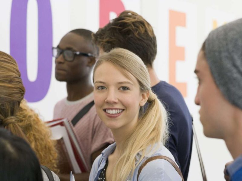 Portrait of university student standing in corridor, students talking in background Portrait of university student standing in corridor, students talking in background
