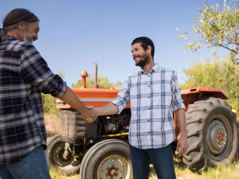 Happy friends shaking hands in farm on a sunny day