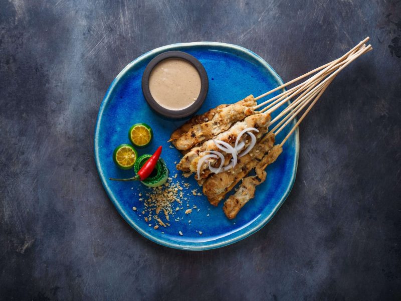 Indonesian chicken skewers sate with peanut sauce and salad, top view, copyspace.